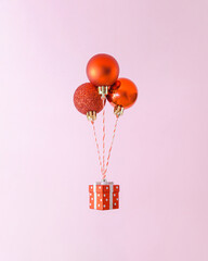 Creative composition with levitating three red Christmas decorations and giftbox. Trendy holiday shopping concept.