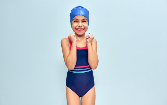 Studio image of a little funny happy girl in a swimsuit, isolated over blue studio background. A positive kid in swimwear making joyful gestures during wins swimming contest.
