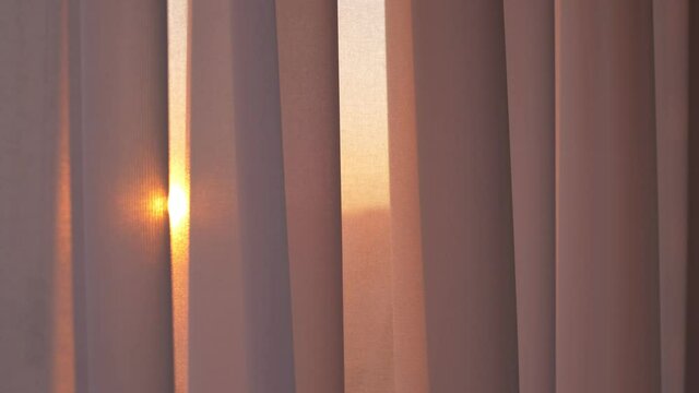 The window is covered with a white tulle curtain. Tulle curtains add coziness and comfort to the home. The kind sunlight of the setting sun seeps through the tulle curtain. The tulle sways gently.