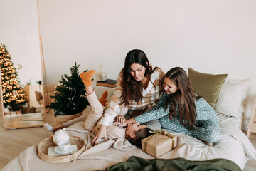 A happy mom with two daughters is resting, relaxing and having fun sitting on the bed in a cozy decorated bedroom during the Christmas holiday at home during the New Year vacations. Selective focus