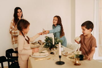 Christmas concert. Children help their mother to set the table. A large family with one parent is preparing for the Christmas holiday in a decorated room during the New Year holidays. Selective focus