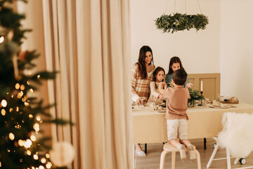 Christmas concert. Children help their mother to set the table. A large family with one parent is preparing for the Christmas holiday in a decorated room during the New Year holidays. Selective focus
