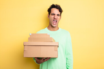 young handsome man shouting aggressively, looking very angry. package boxes