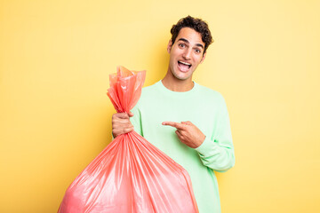 young handsome man looking excited and surprised pointing to the side. trash bag concept