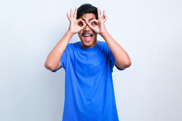 Fototapeta premium Young handsome man wearing casual shirt doing ok gesture like binoculars sticking tongue out
