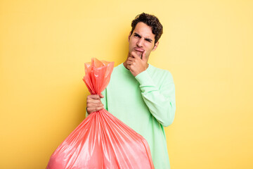 young handsome man thinking, feeling doubtful and confused. trash bag concept