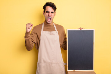 young handsome man shouting aggressively with an angry expression. chef and blackboard concept