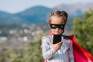 Brave girl in superhero costume browsing on smartphone