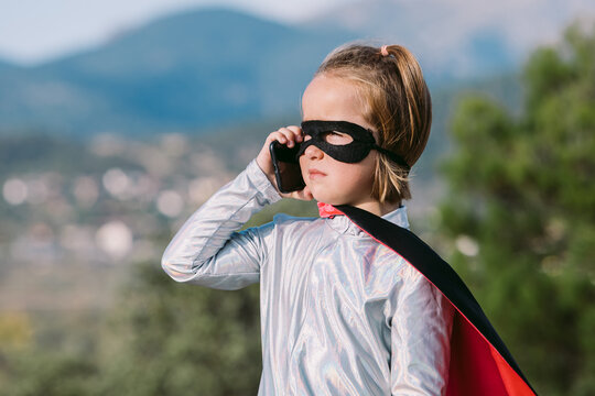Brave girl in superhero costume talking on smartphone