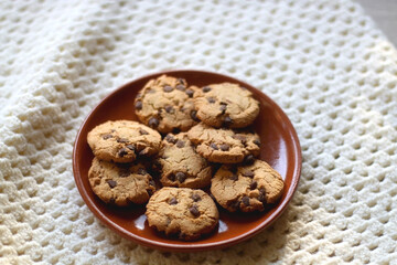 Plate of chocolate chip cookies and knitted blanket. Hygge at home. Selective focus.