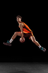 Full length portrait of basketball player training isolated on dark studio background. Tall...