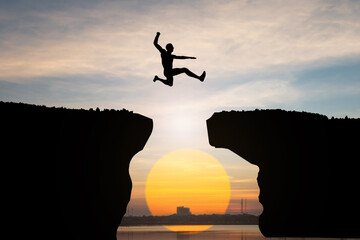 silhouette of Man jump through the gap between hill on sunset background, business concept idea