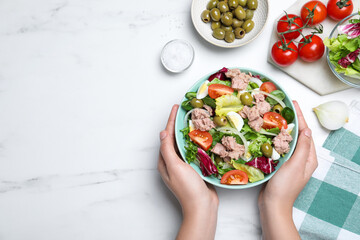 Woman holding bowl of delicious salad with canned tuna at white table, top view. Space for text