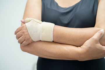 Asian middle-aged lady woman use elastic bandage to treating De Quervain syndrome at hand and finger in office.
