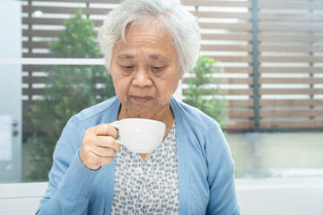 Asian senior or elderly old woman patient holding mug and drinking coffee in the morning at home,  healthy strong medical concept