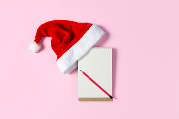 New year wish list concept. Notepad, Santa Claus hat isolated on pink background. Holiday banner...