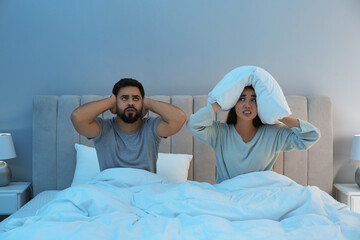 Young couple suffering from noisy neighbours in bed at home - obrazy, fototapety, plakaty