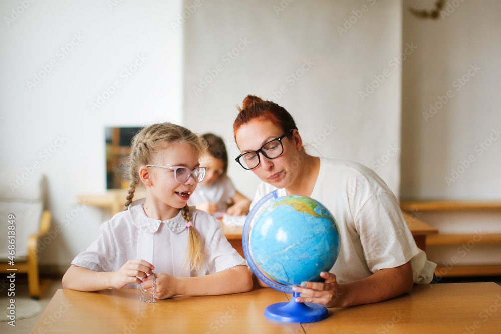 Wall mural a teacher and a girl, a student, a child at school at a desk working with a globe, a teacher and a student are studying geography, looking for countries on the map. , modern education and technology