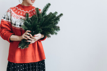 a modern woman in a red sweater with fir branches in her hands at Christmas on a light background. The minimum concept of the new year.copyspace