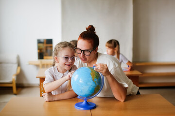 a teacher and a girl, a student, a child at school at a desk working with a globe, a teacher and a student are studying geography, looking for countries on the map. , modern education and technology