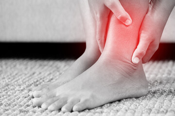 A woman suffering from feeling knee pain sitting sofa at home. hand massaging her painful knee. Health care and medical concept.