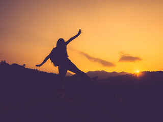 Fototapeta na wymiar Silhouette of happy woman with open arms on peak of mountain at sunset.