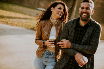 Young couple walking in autumn park with coffee to go cups in hands