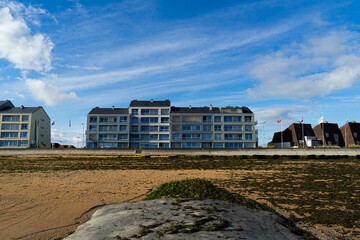 Obraz premium Immeuble en bord de mer sous un ciel bleu et nuageux, devant une plage de sable et d'algues.