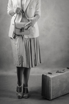 A woman dressed in retro style with a suitcase at her feet and a handbag in her hands. Fragmented black and white image