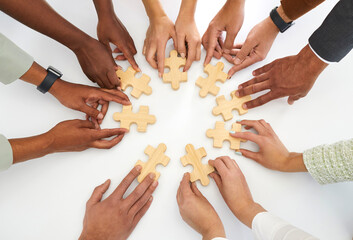 Concept background with diverse multiracial group of young people joining parts of jigsaw puzzle on white table as metaphor for business team and teamwork. Cropped shot of hands holding jigsaw pieces