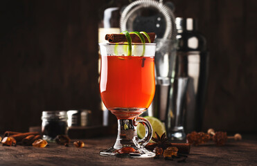 Hot punch, grog, winter warming cocktail drink with dark rum, port, honey, lime juice, tea, cinnamon and cloves in glass on vintage wooden background in autumn decoration