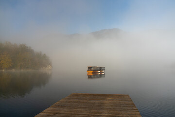wooden motorboat on a calm lake on a foggy morning with a wooden dock in the foreground