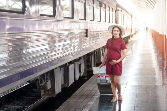 Asian woman pregnant in red dress holding a map with red suitcase  at railway station travel,traveler with backpack in summer Holiday concept Thailand