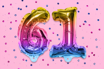 Rainbow foil balloon number, digit sixty one on a pink background with sequins. Birthday greeting...