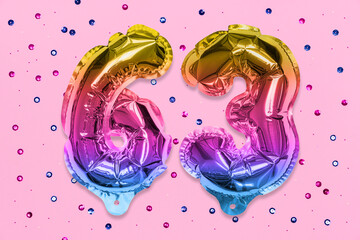 Rainbow foil balloon number, digit sixty three on a pink background with sequins. Birthday greeting card with inscription 63. Top view. Numerical digit. Celebration event, template.