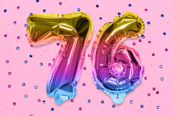 Rainbow foil balloon number, digit seventy six on a pink background with sequins. Birthday greeting card with inscription 76. Top view. Numerical digit. Celebration event, template.