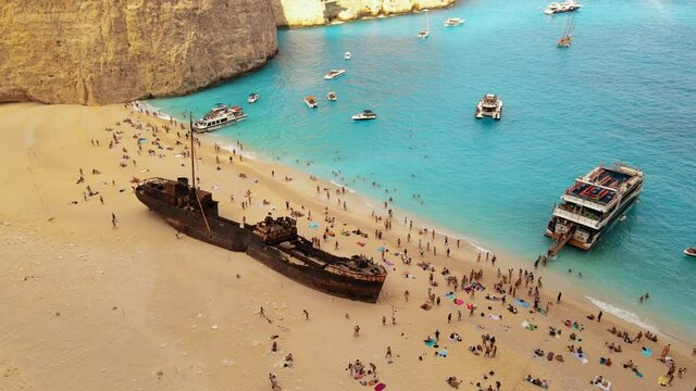 Aerial drone view of the Navagio beach on the Ionian Sea coast of Zakynthos, Greece. Moored boats and resting people, rusty ship, blue water. Slow motion