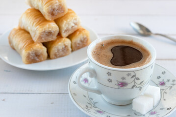 A cup of frothy coffee and a plate of baklava for breakfast.