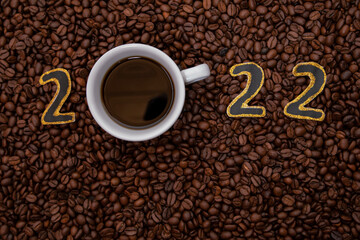 Naklejka premium 2022. New Year black and gold numbers with coffee mug, cup. With a lots of coffee beans around. Coffee background. Holiday concept.
