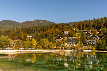 Fototapeta na wymiar mountain cottages and holiday homes on the shores of Lake Jasna in beautiful autumn colors forest in northern Slovenia