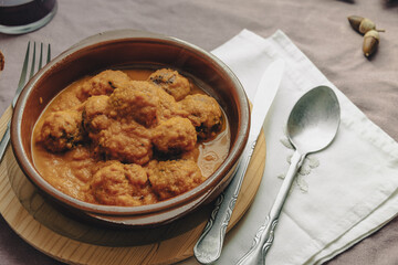 Rustic plate of meatballs in tomato sauce set on a tablecloth.