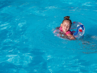 Little girl with colorful inflatable ring in the pool with blue clear water.