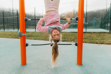 A young girl on a climbing frame hangs upside down on a children's playground.