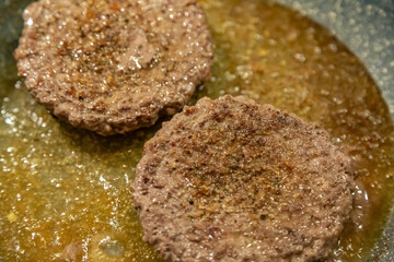 Juicy minced beef patties are fried in oil in a frying pan on a gas stove