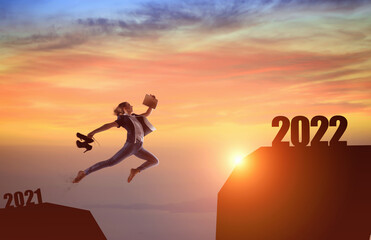 Silhouette woman jumping between cliff with number 2021 to 2022 and birds flying at tropical sunset beach.
