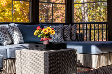 Cozy patio corner in a screened porch with flower bouquet in a vase, autumn leaves and woods in the...