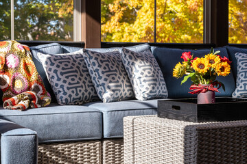 Cozy patio corner in a screened porch with flower bouquet in a vase, autumn leaves and woods in the background.