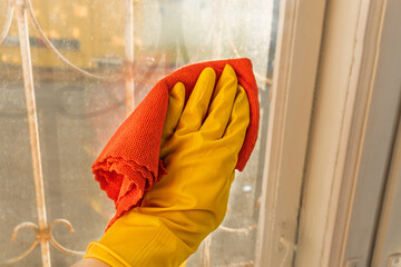 a hand in a yellow rubber protective glove holds a cleaning rag and washes the dirty window with it. Selective focus. Indoor cleaning at home. Washing windows. Indoor cleaning at home. Washing windo

