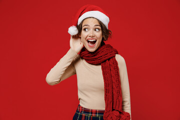 Young smiling curious woman 20s in Santa Claus Christmas red hat try to hear you overhear listening...