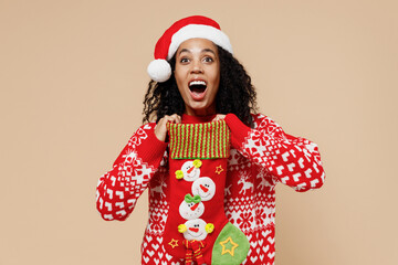 Amazed young african american Santa woman in Christmas hat sweater hold decorative stocking...